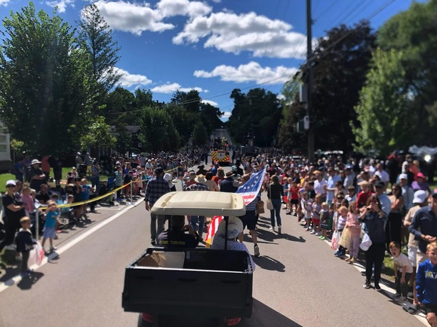A golf cart carries a flag bearer down Franklin Road as crowds line both sides of the street for the Labor Day parade.