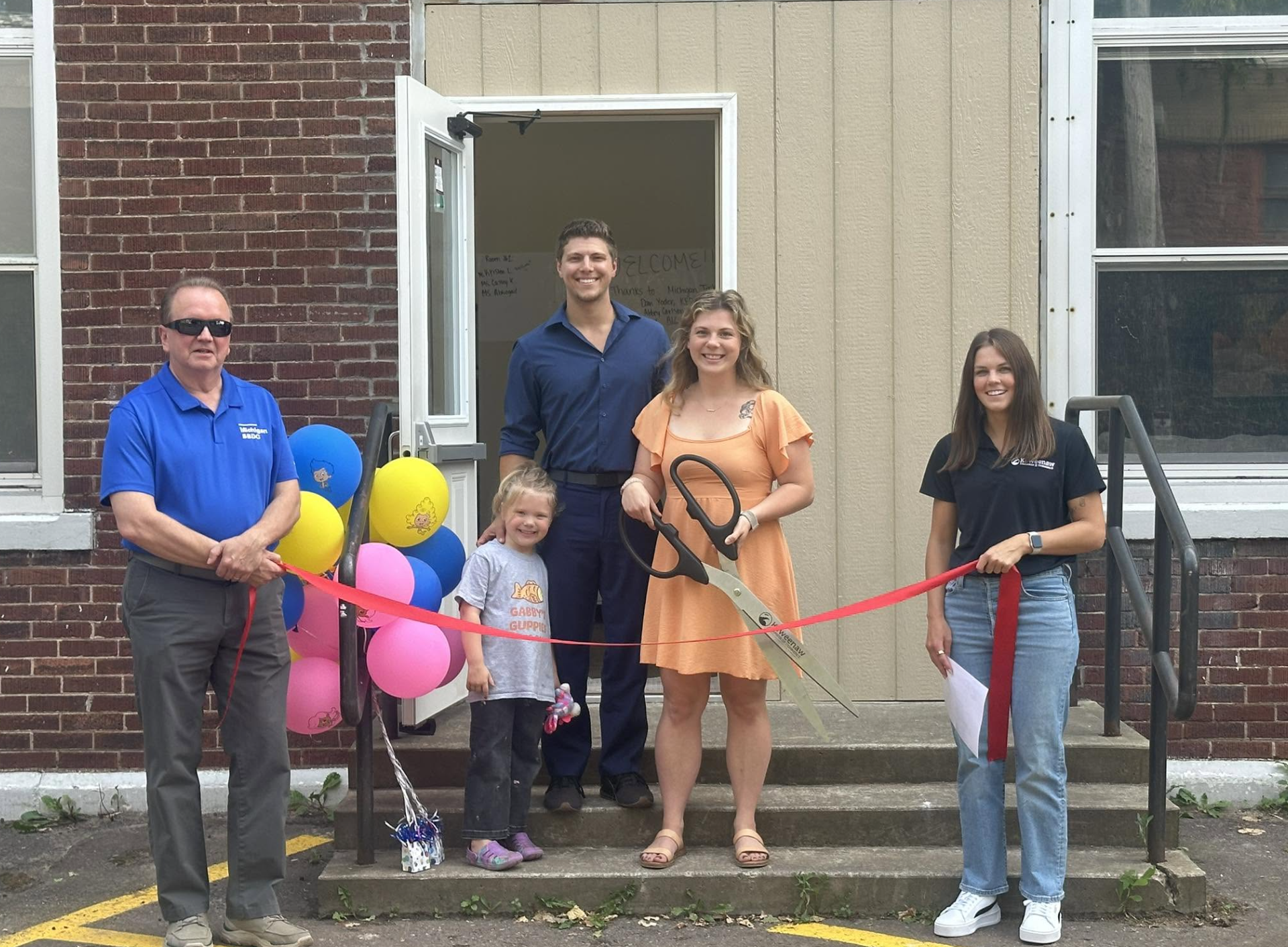 Officials from Michigan SBDC and the Keweenaw Economic Development Alliance join Gabby's Guppies staff and a child for a ribbon-cutting ceremony outside the Hancock childcare center.