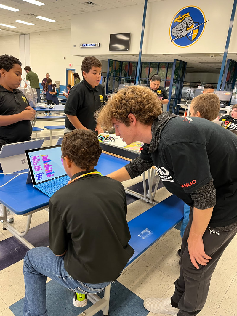 BotTanks members help students working on a laptop during a STEM outreach activity.