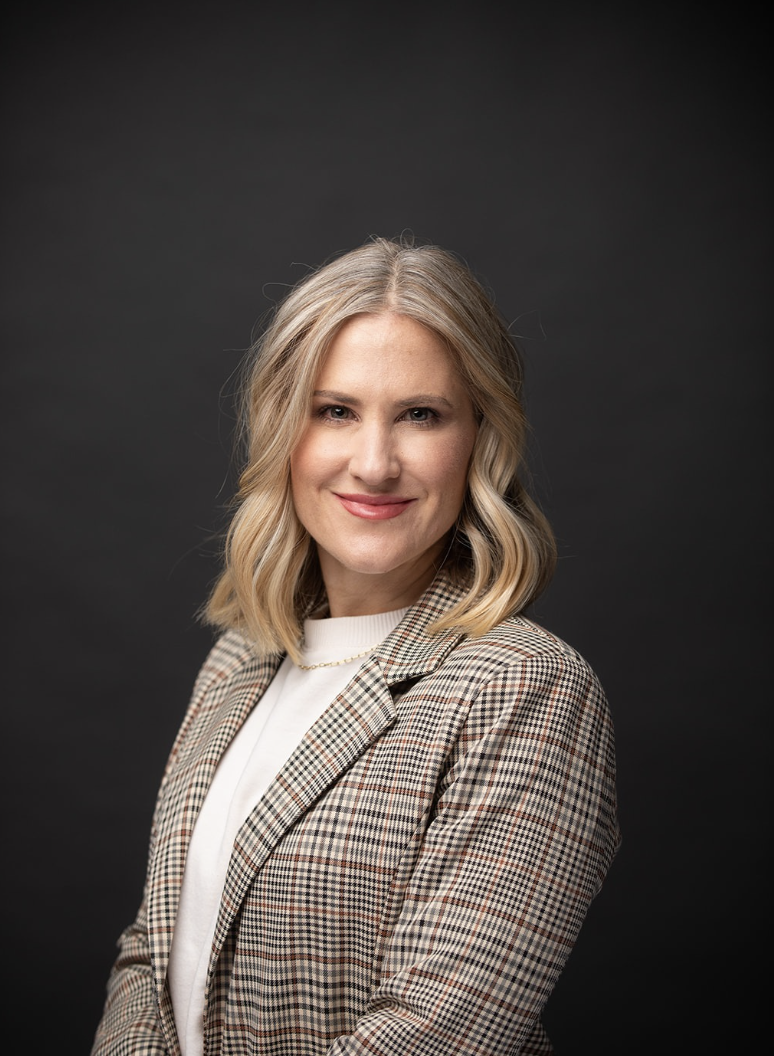 Jennifer Jacobson poses for a portrait against a dark background wearing a plaid blazer.