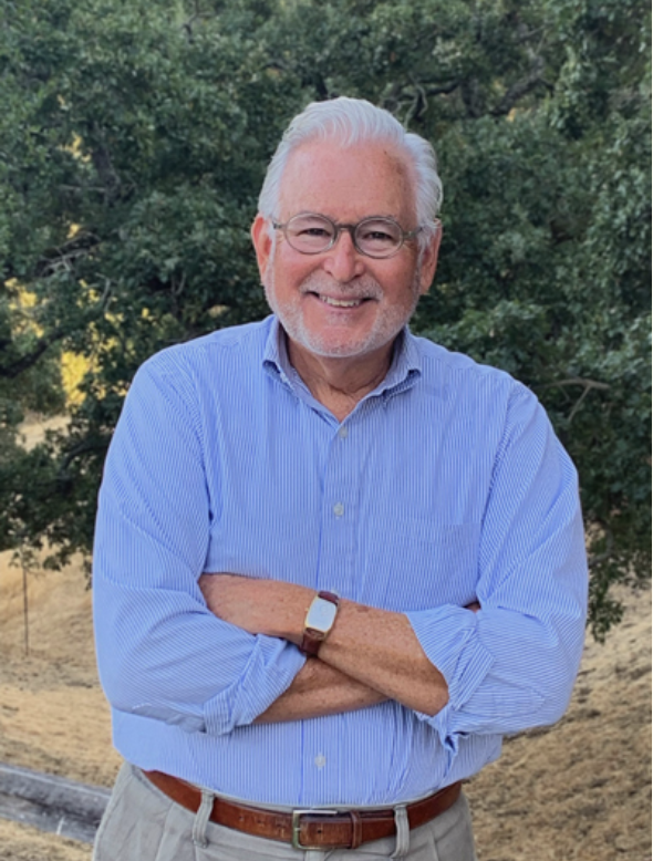 Jim Cervantes smiling outdoors with his arms crossed, wearing glasses and a blue striped shirt.