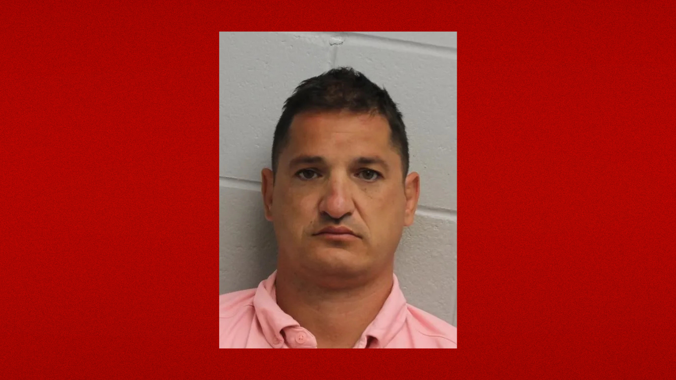 Portrait of a man wearing a pink collared shirt against a cinder block wall.