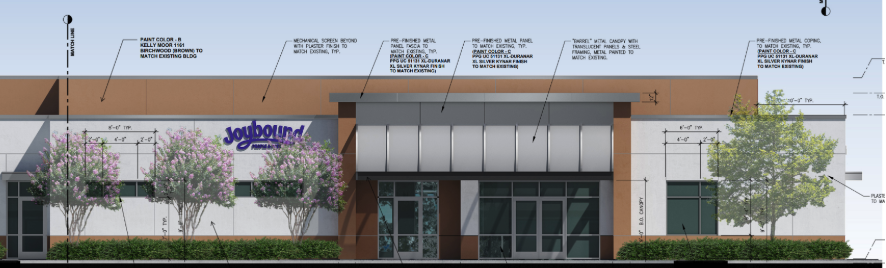 Architectural elevation rendering of the proposed Joybound daycare building's front facade, showing a metal canopy entrance, storefront glazing, and the Joybound sign, with material and paint-color callouts labeled around the exterior.