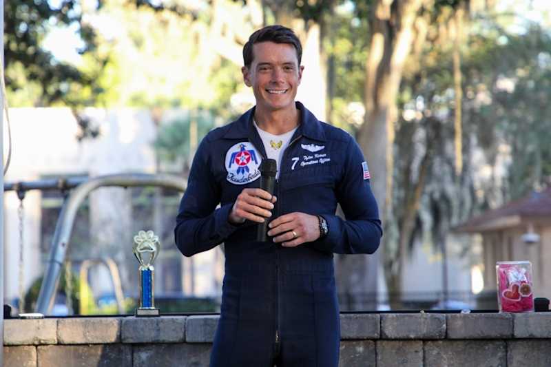 Lt. Col. Tyler Keener in his Thunderbirds flight suit holds a microphone during his visit to Bolles.