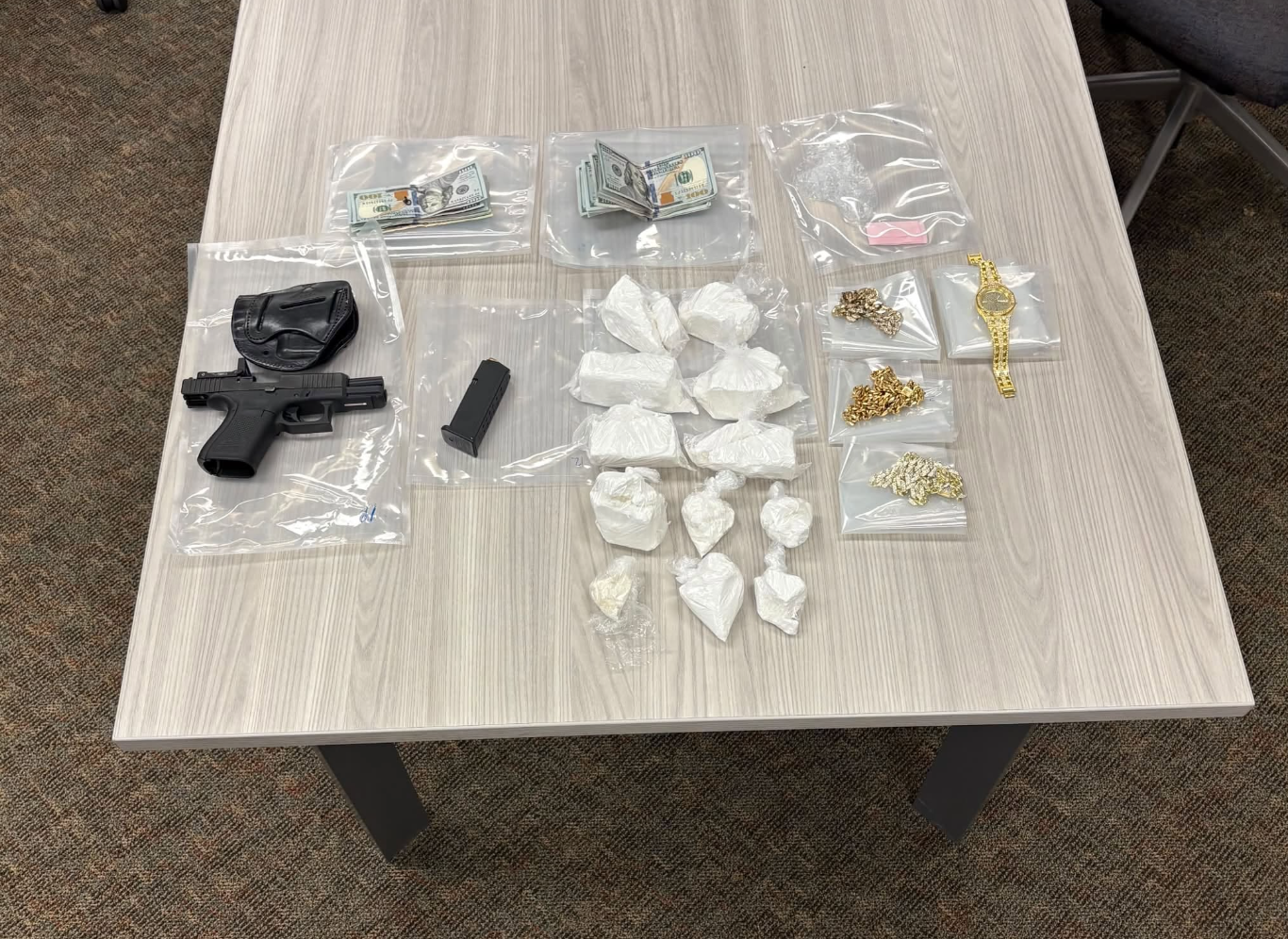 Evidence photo from Lansing police showing seized items laid out on a table, including bundles of cash, more than 1,000 grams of suspected cocaine in plastic bags, a handgun with holster and magazine, and gold jewelry including chains, rings and a watch.