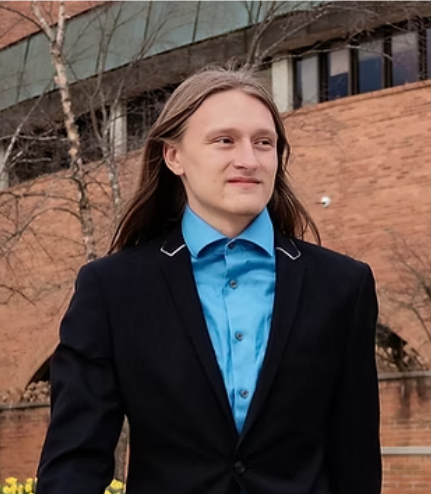 Lyndon Dibble wears a black blazer and blue shirt outside a brick building.