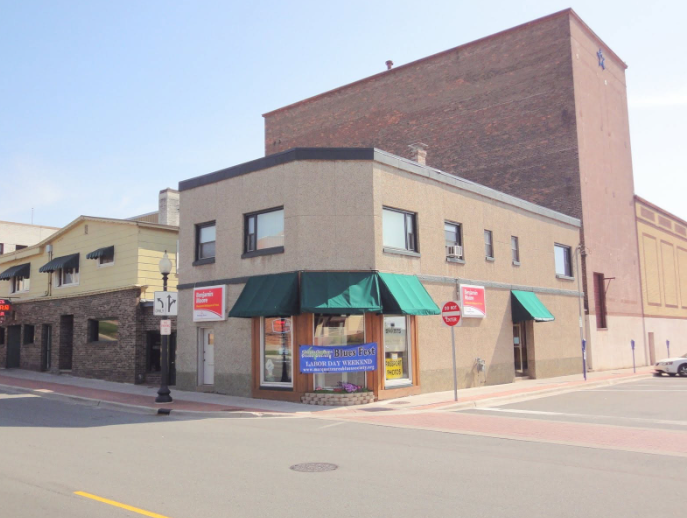 Corner commercial building with green awnings and a large brick structure behind it.
