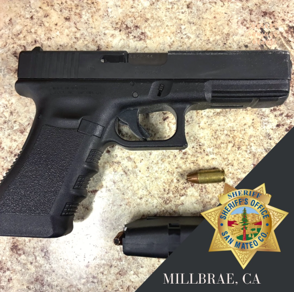 A black Glock 17 handgun, a loaded round, and a magazine on a countertop, next to the San Mateo County Sheriff's Office badge and text reading "Millbrae, CA."
