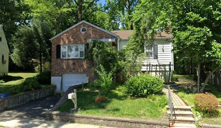 A single-family home with a brick exterior, front yard, driveway and walkway surrounded by mature trees and greenery.