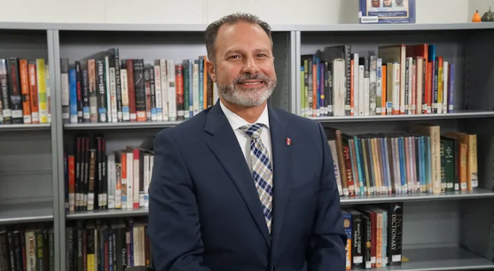 Rochester Community Schools Superintendent Nicholas Russo smiles while standing in front of bookshelves in a school media center.
