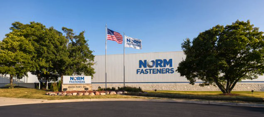 The Norm Fasteners facility in Plymouth, Michigan, with the company's signage on the building exterior and at the entrance, American flag flying alongside a company flag.