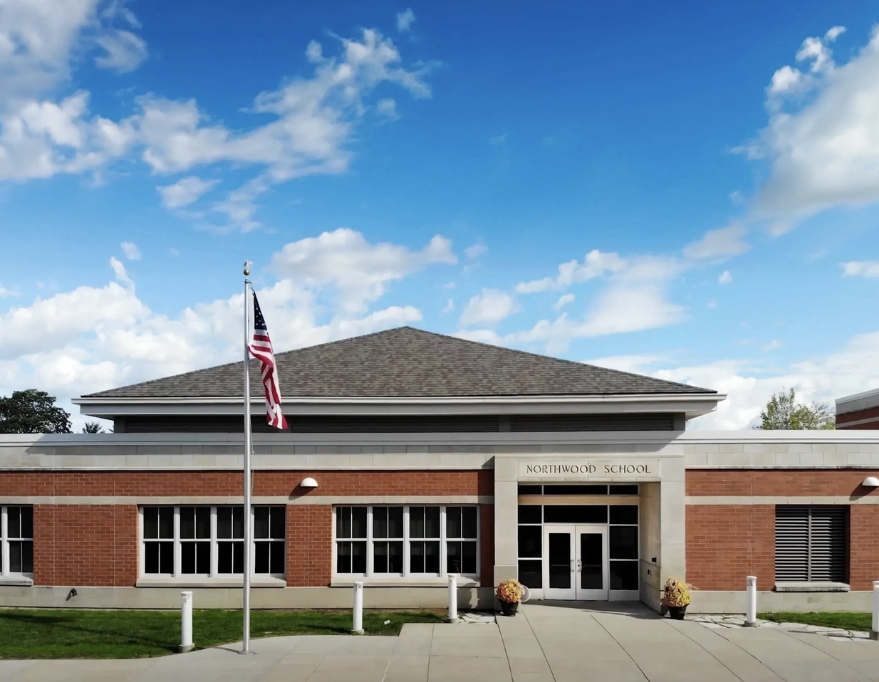 Northwood School’s brick entrance with an American flag, front walkway and blue sky.