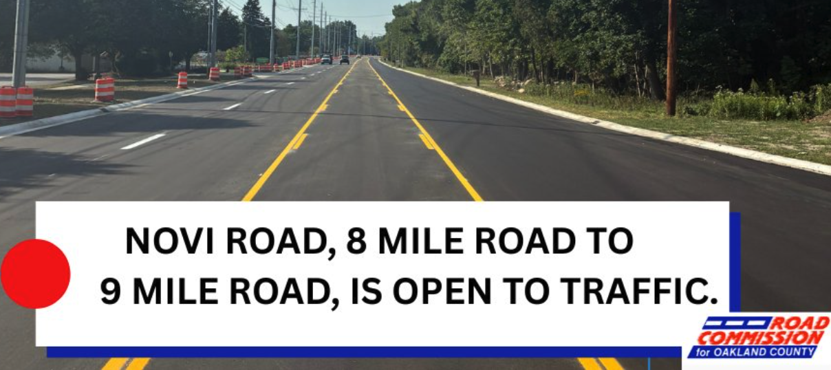Newly paved Novi Road between 8 Mile and 9 Mile roads, lined with traffic cones, with a graphic reading "Novi Road, 8 Mile Road to 9 Mile Road, is open to traffic."