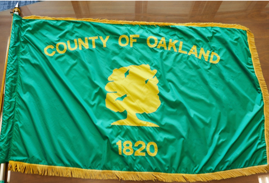 Green Oakland County flag with a maize-colored oak tree, “County of Oakland” lettering and “1820” in yellow.