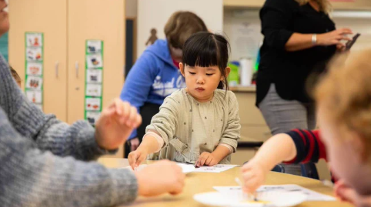 A young girl works at a table with a coloring activity alongside other preschool-age children in a classroom at Oakland University's Lowry Center.