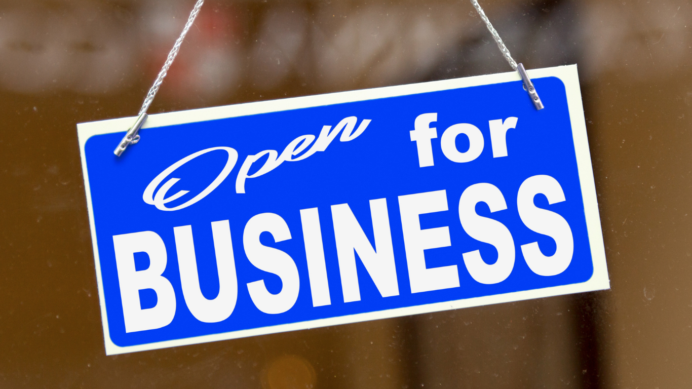 Blue open for business sign hanging on front window of building.
