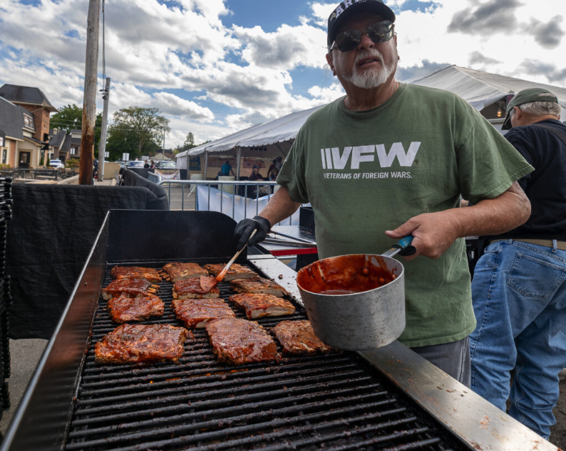 A VFW volunteer brushes barbecue sauce onto racks of ribs cooking on a grill during the Plymouth Fall Festival.