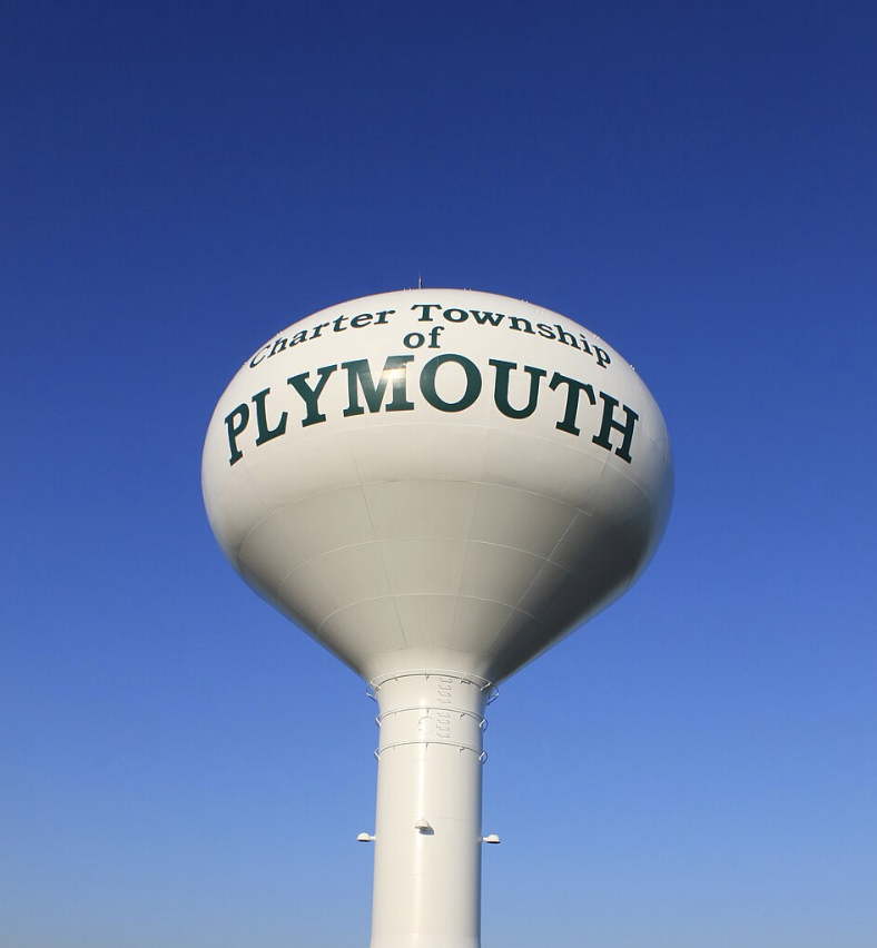A white water tower reading "Charter Township of Plymouth" against a clear blue sky.