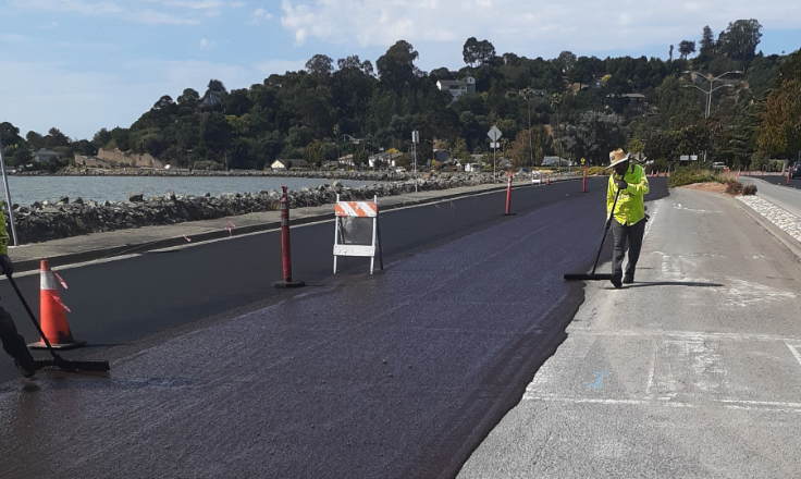 A worker in a safety vest rakes fresh asphalt during repaving of Point San Pedro Road along the Marin County shoreline.