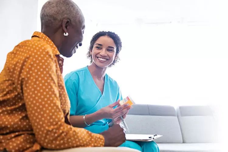 Nurse sitting with a patient holding a pill bottle.