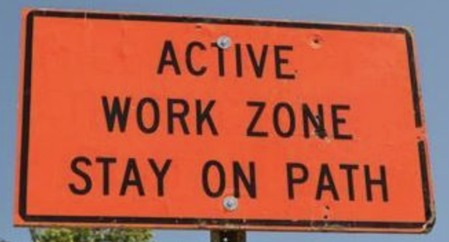 Orange "Active Work Zone – Stay on Path" road sign against a blue sky, posted by the Road Commission for Oakland County.
