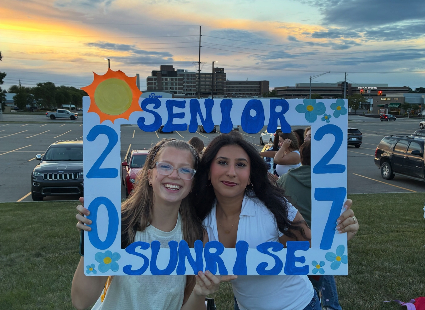 Two Rochester High School seniors smile while holding a hand-painted "Senior Sunrise 2027" photo frame at sunrise.
