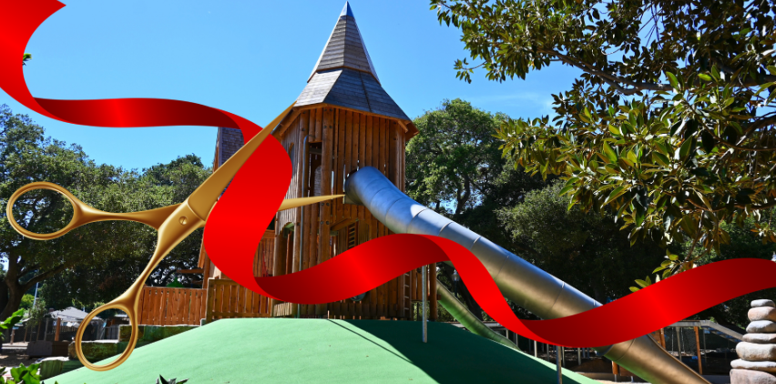 Wooden playground tower with a metal tube slide, overlaid with a red ribbon and gold scissors.