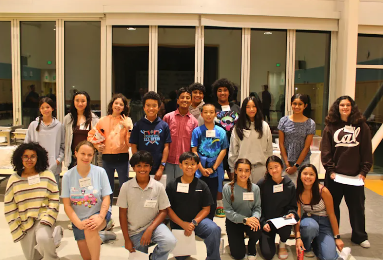 Students pose in two rows inside a school room, with several seated in front.
