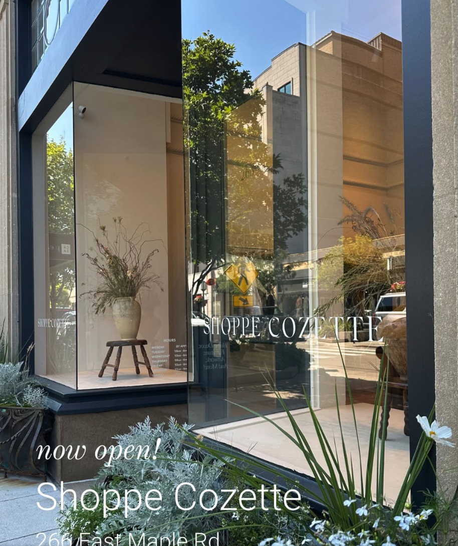 Shoppe Cozette storefront in downtown Birmingham with large glass windows, plants and a “now open” message over the image.