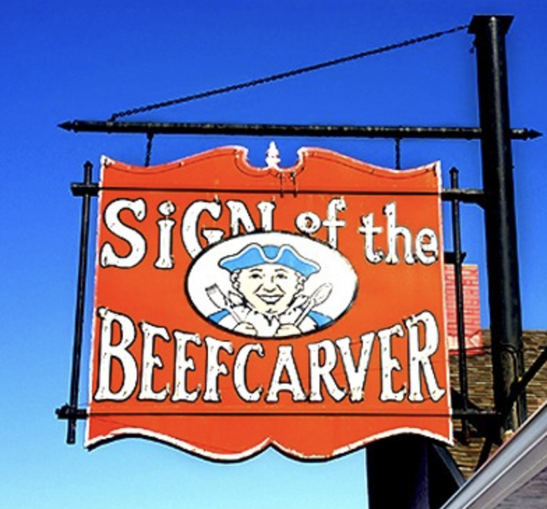 Red Sign of the Beefcarver sign hanging against a blue sky.