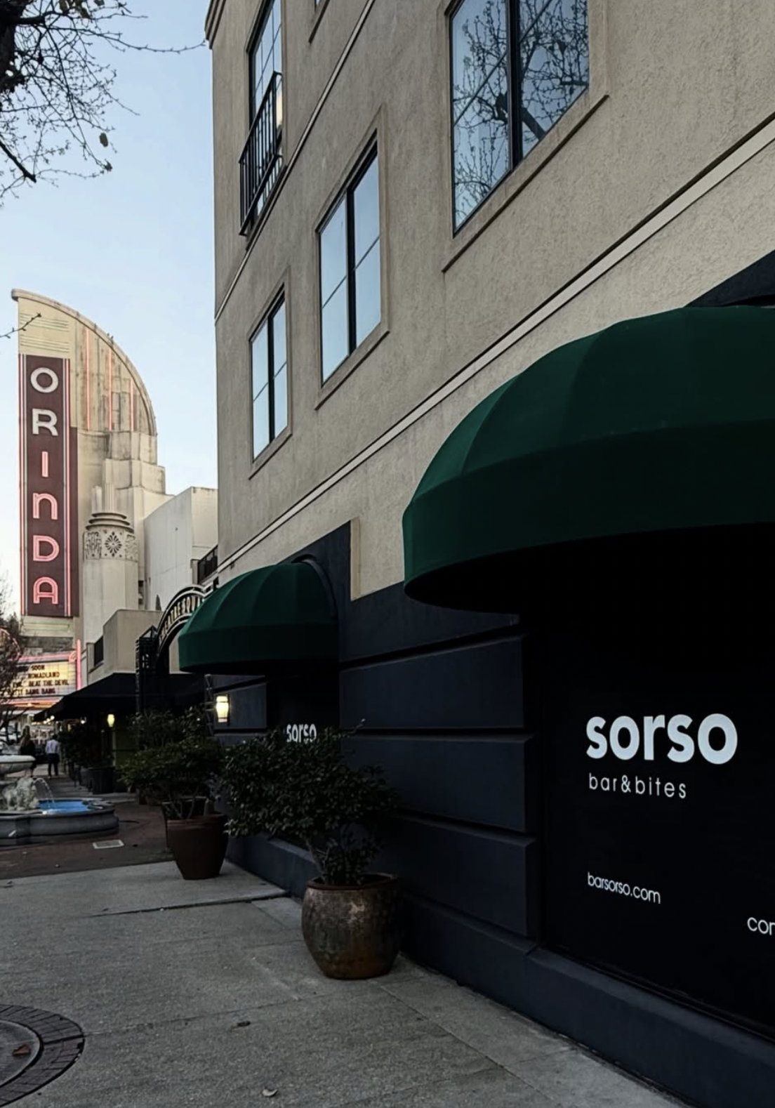 Storefront of Sorso Bar & Bites in downtown Orinda, showing a black facade with green scalloped awnings and white "sorso bar&bites" signage, with the Orinda Theatre's vertical marquee visible down the block.