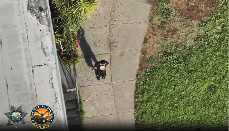 An aerial drone view shows a person walking on a sidewalk near a palm tree and stairway, with San Rafael Police Department and Drone as First Responder Unit logos overlaid in the corner.