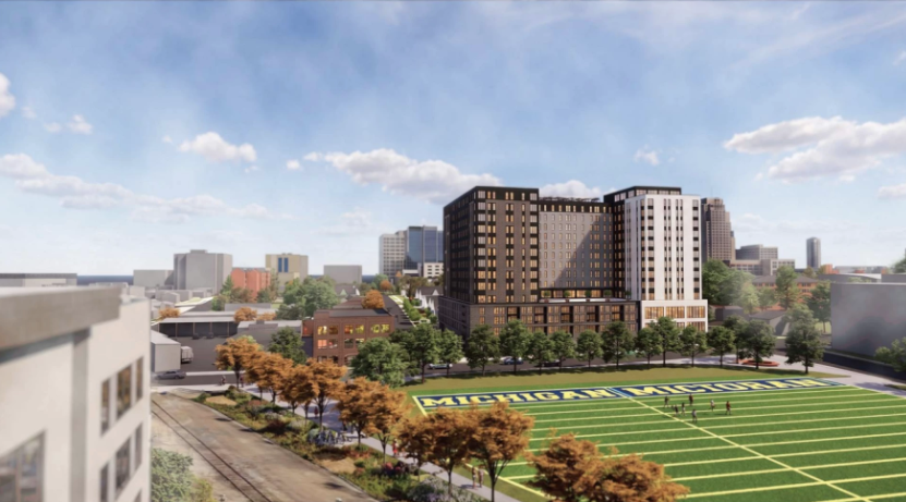 Architectural rendering of The Dean, a 14-story residential tower with a mix of dark brick and light stone facades, overlooking the University of Michigan's Elbel Field practice field and the Ann Arbor skyline.