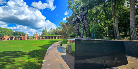A memorial honoring military service, set in a landscaped park with trees, walkways and open green space.