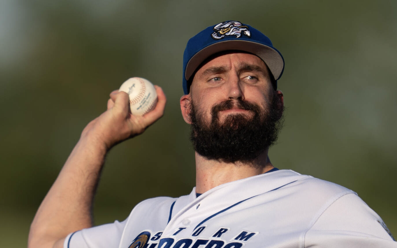 Tony Gonsolin, wearing an Omaha Storm Chasers cap and jersey, winds up to throw a baseball.