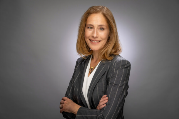 Professional headshot of C. Cybele Raver, wearing a gray pinstripe blazer, arms crossed, smiling against a gray backdrop.