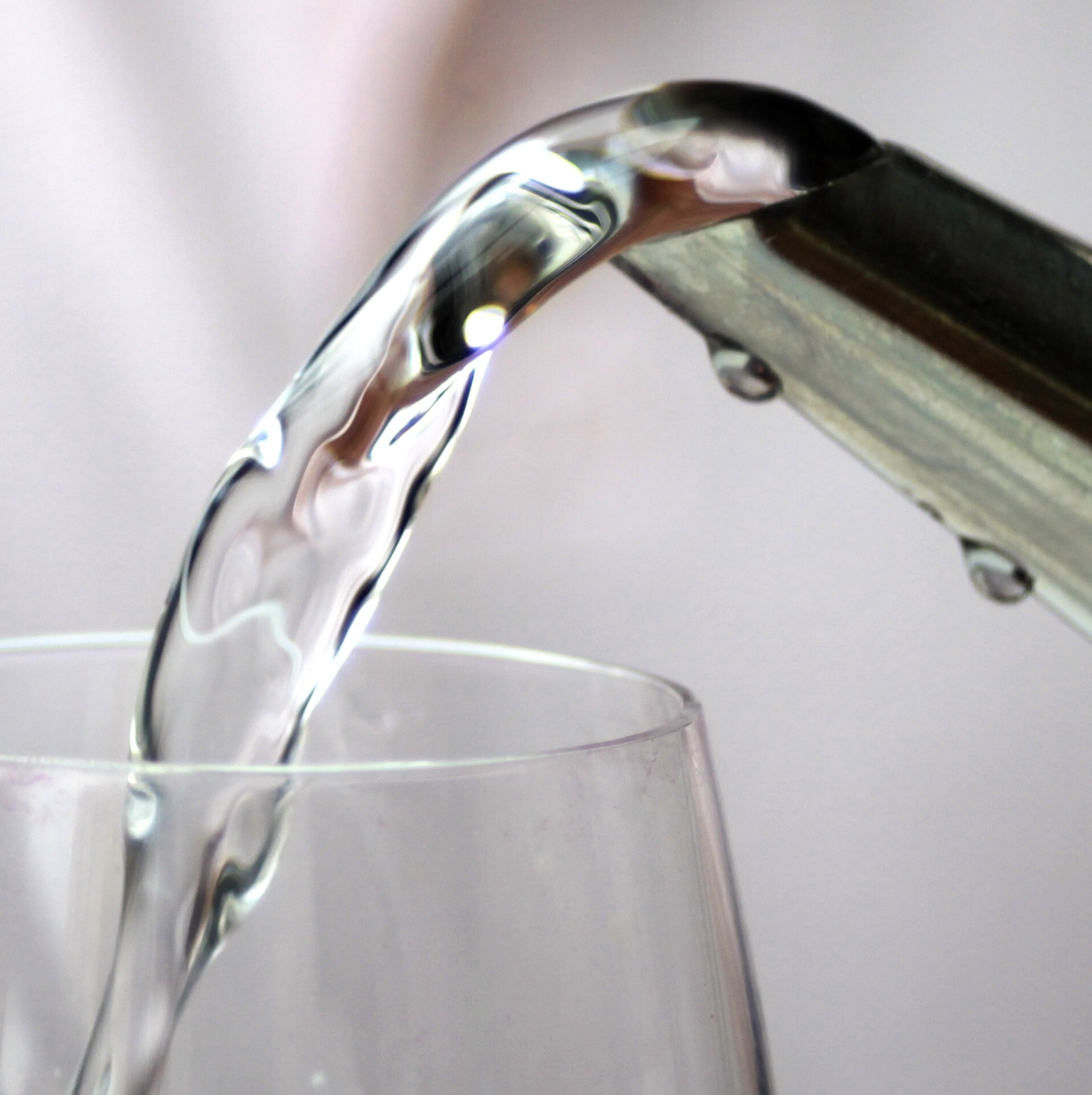 Water pours from a metal pitcher into a clear glass.