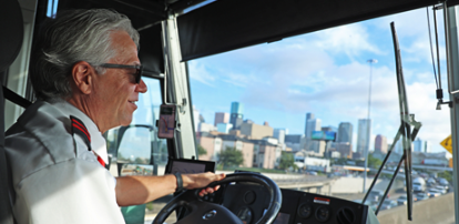 A Woodlands Express bus driver navigates the highway toward downtown Houston, its skyline visible through the windshield.